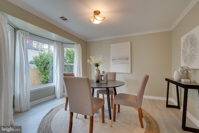 dining room featuring light wood-style flooring, baseboards, visible vents, and ornamental molding