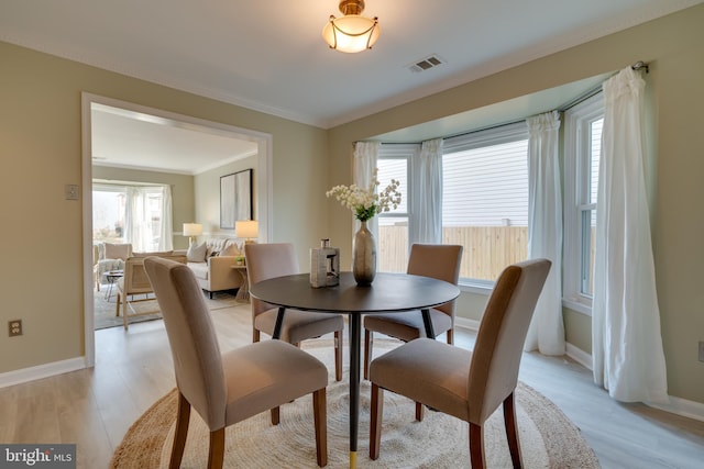 dining space featuring light wood-type flooring, visible vents, baseboards, and ornamental molding