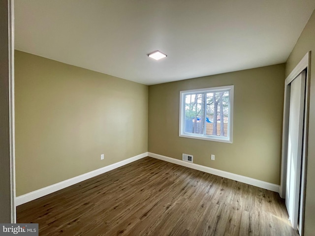 unfurnished bedroom with dark wood finished floors, visible vents, a closet, and baseboards