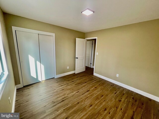 unfurnished bedroom featuring wood finished floors, baseboards, and a closet