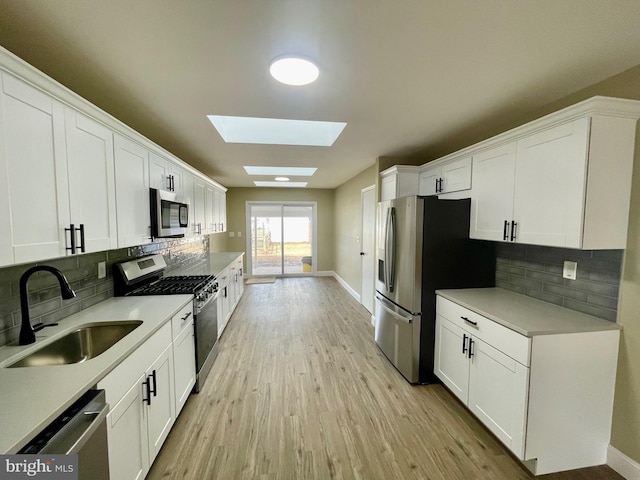 kitchen featuring a skylight, a sink, stainless steel appliances, white cabinets, and light wood-style floors