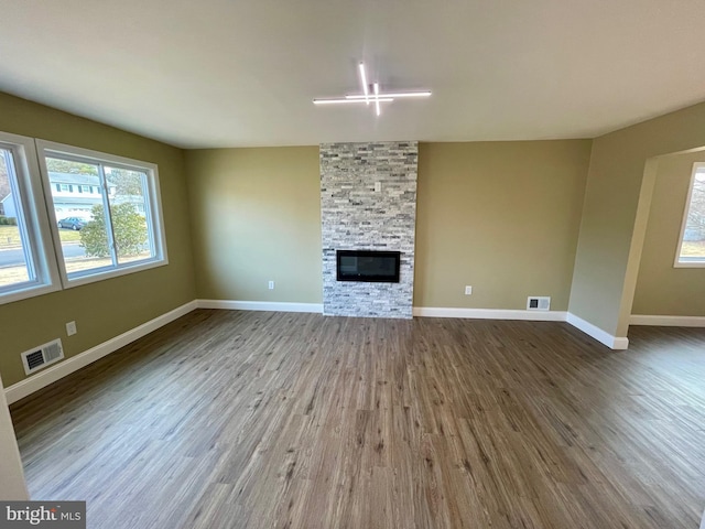 unfurnished living room featuring visible vents, a stone fireplace, baseboards, and wood finished floors