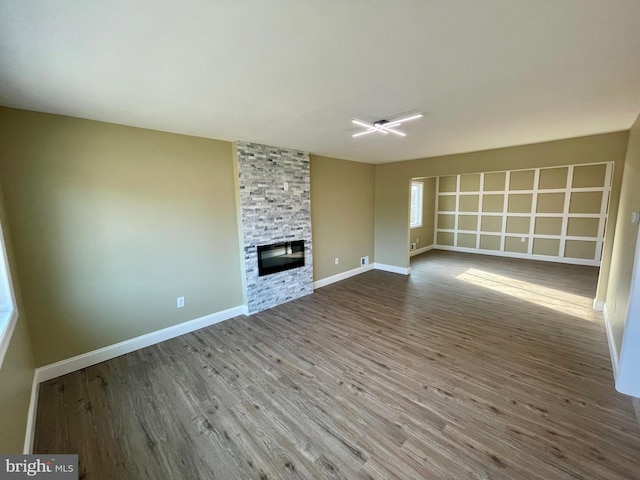 unfurnished living room featuring a stone fireplace, baseboards, and wood finished floors