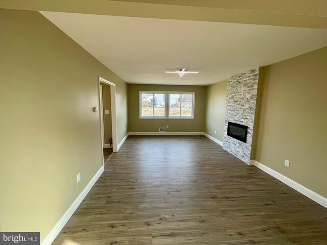 unfurnished living room featuring a stone fireplace, dark wood-type flooring, and baseboards