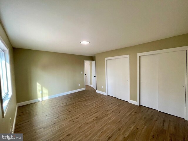 unfurnished bedroom with baseboards, two closets, and wood finished floors