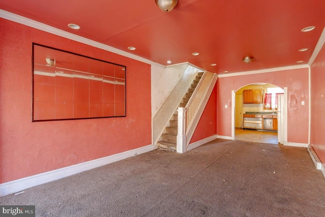 unfurnished living room featuring stairway, baseboards, arched walkways, crown molding, and carpet flooring