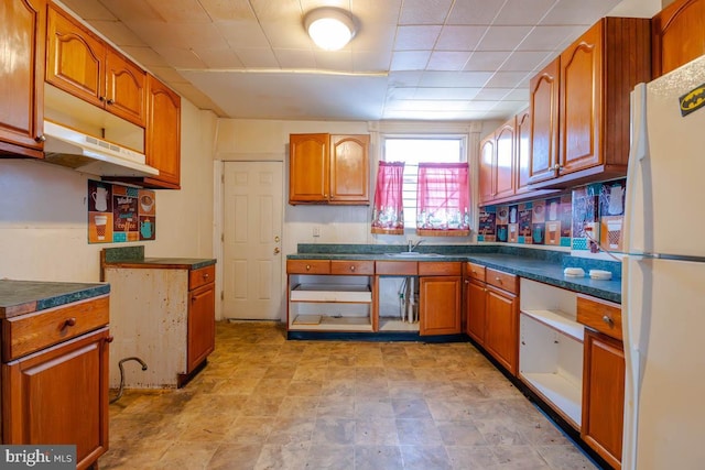 kitchen with dark countertops, brown cabinetry, and freestanding refrigerator