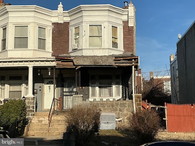 view of front of house featuring brick siding, fence, and covered porch