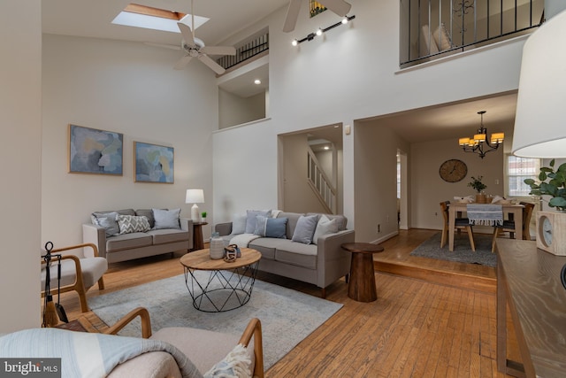 living area with stairway, ceiling fan with notable chandelier, a skylight, and wood-type flooring