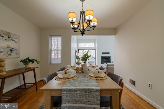 dining area with visible vents, baseboards, light wood-style flooring, a fireplace, and a notable chandelier