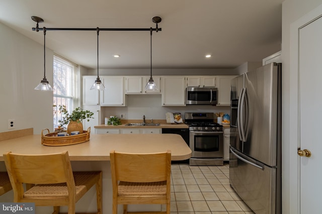 kitchen featuring light tile patterned floors, a peninsula, white cabinets, stainless steel appliances, and a sink