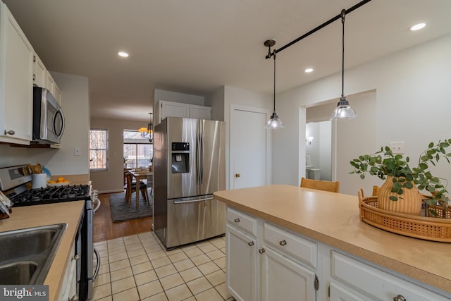 kitchen featuring hanging light fixtures, appliances with stainless steel finishes, white cabinetry, and a sink