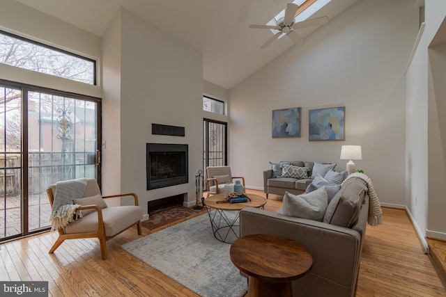 living area featuring high vaulted ceiling, light wood-style floors, a fireplace, baseboards, and ceiling fan