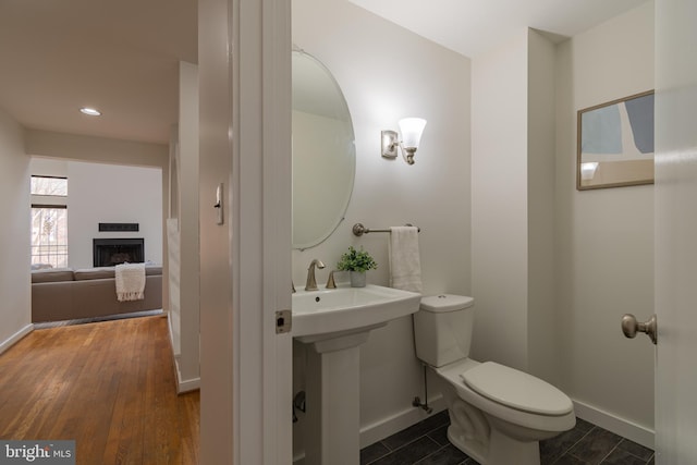 half bath with a fireplace, toilet, baseboards, and wood finished floors