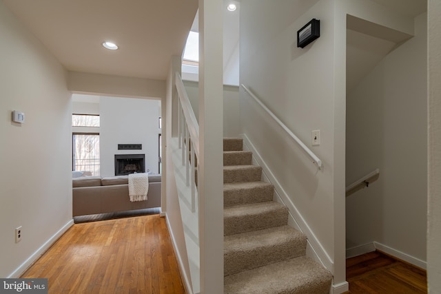 stairway featuring hardwood / wood-style floors, recessed lighting, a fireplace, and baseboards