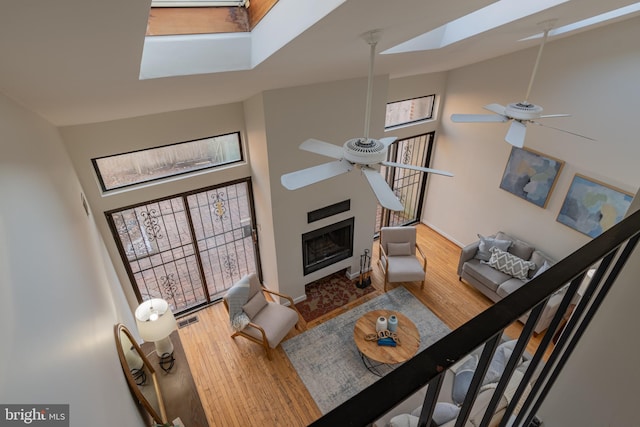 living room featuring a ceiling fan, wood finished floors, high vaulted ceiling, a skylight, and a fireplace