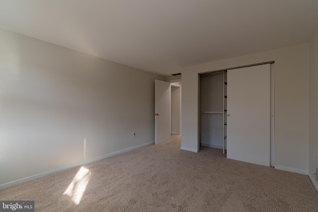 unfurnished bedroom with a closet, light carpet, and baseboards