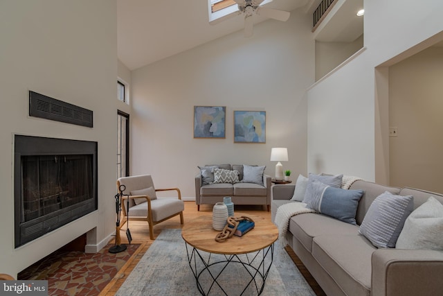 living area featuring a fireplace with flush hearth, baseboards, a high ceiling, and ceiling fan