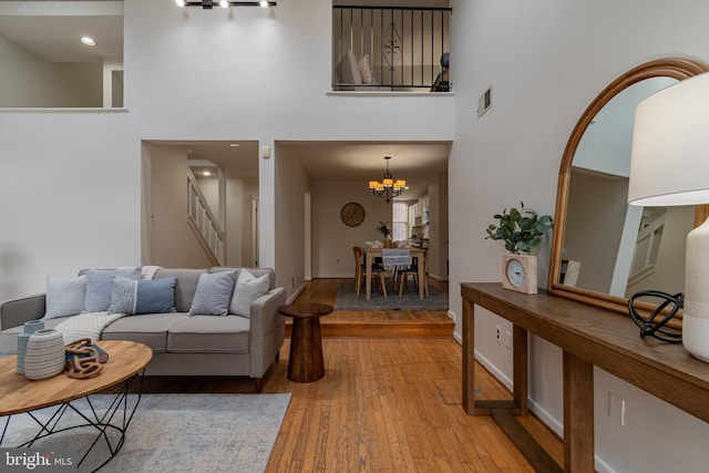 living area featuring stairway, light wood-style floors, an inviting chandelier, and a towering ceiling