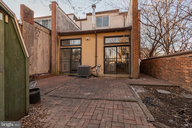 back of house featuring central AC unit, a chimney, a patio, and stucco siding