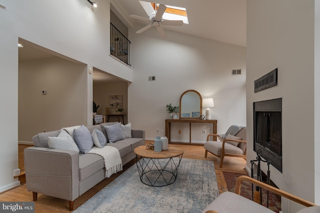 living room with visible vents, a ceiling fan, a skylight, a fireplace, and light wood finished floors