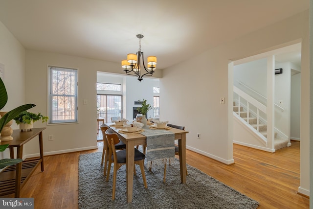 dining area with an inviting chandelier, light wood-type flooring, stairs, and baseboards