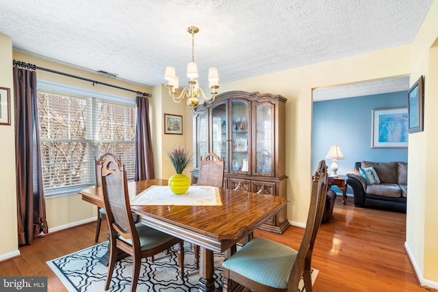 dining space with visible vents, a textured ceiling, an inviting chandelier, and wood finished floors