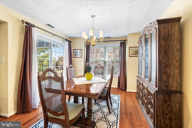 dining space featuring light wood-type flooring, visible vents, a textured ceiling, baseboards, and a chandelier