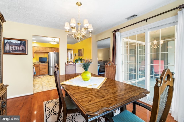 dining room featuring an inviting chandelier, light wood-style flooring, visible vents, and a textured ceiling