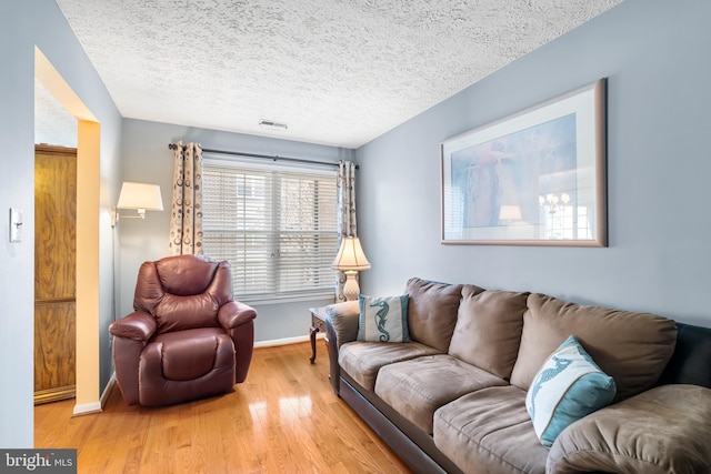 living room with visible vents, wood finished floors, baseboards, and a textured ceiling