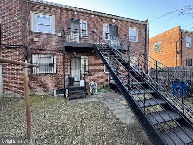 rear view of property with brick siding, stairs, and fence