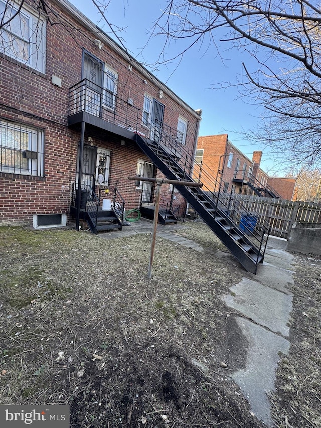 back of property with brick siding, a balcony, and fence