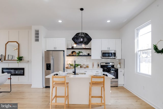 kitchen featuring light wood finished floors, decorative backsplash, a healthy amount of sunlight, and appliances with stainless steel finishes