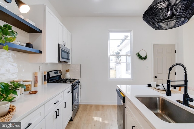 kitchen with open shelves, a sink, white cabinetry, stainless steel appliances, and light countertops