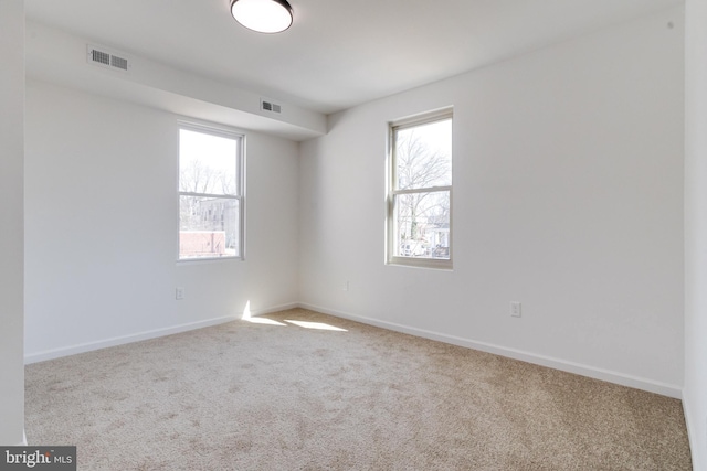 carpeted spare room featuring visible vents, baseboards, and a healthy amount of sunlight