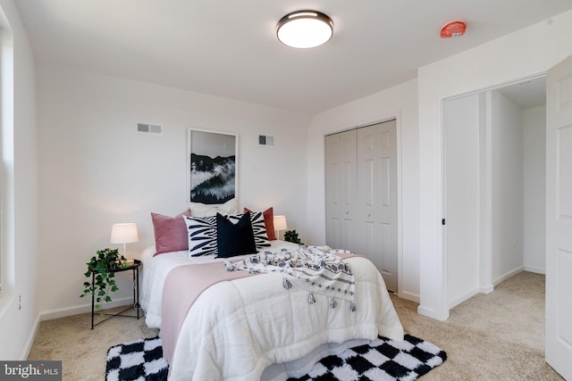 bedroom with a closet, visible vents, light colored carpet, and baseboards