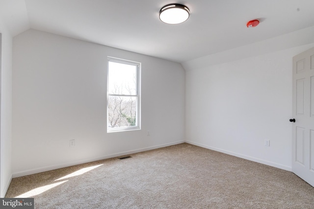 carpeted empty room with visible vents, baseboards, and vaulted ceiling