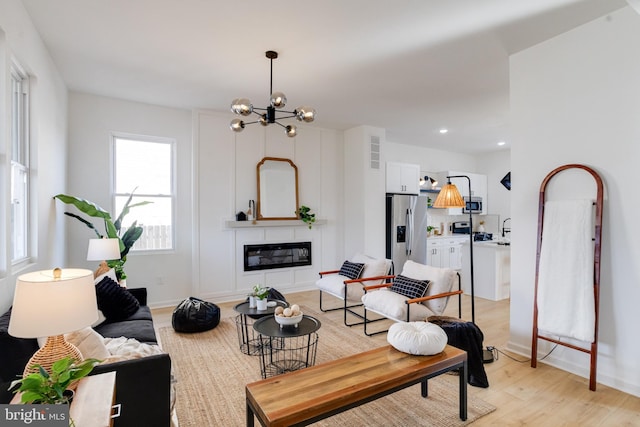 living room featuring light wood-style flooring, a glass covered fireplace, recessed lighting, baseboards, and a chandelier