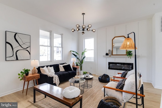 living room featuring light wood-type flooring, baseboards, an inviting chandelier, and a glass covered fireplace