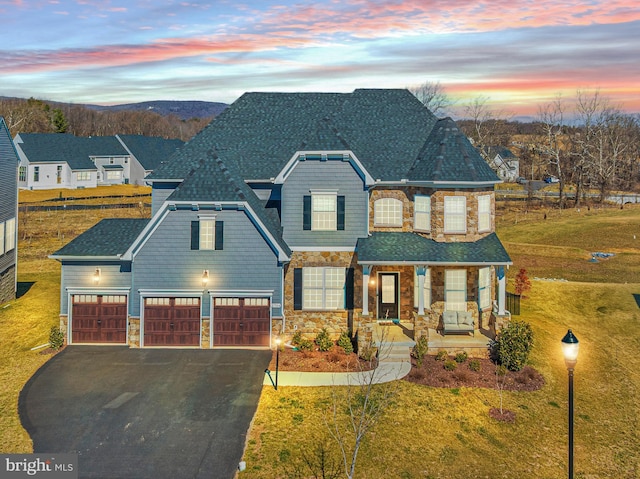 view of front of house with aphalt driveway, an attached garage, stone siding, and a yard