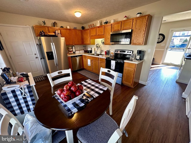 kitchen with brown cabinets, dark wood-type flooring, a sink, stainless steel appliances, and light countertops