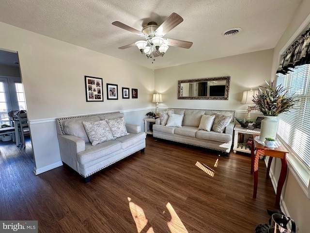 living room featuring ceiling fan, wood finished floors, visible vents, and a textured ceiling