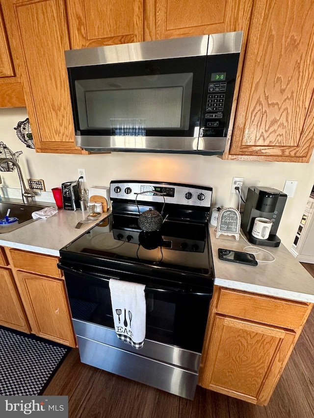 kitchen with dark wood-type flooring, stainless steel microwave, range with electric stovetop, brown cabinetry, and light countertops