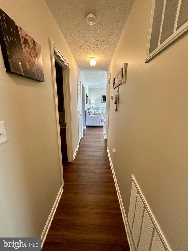 hallway featuring visible vents, baseboards, a textured ceiling, and dark wood finished floors