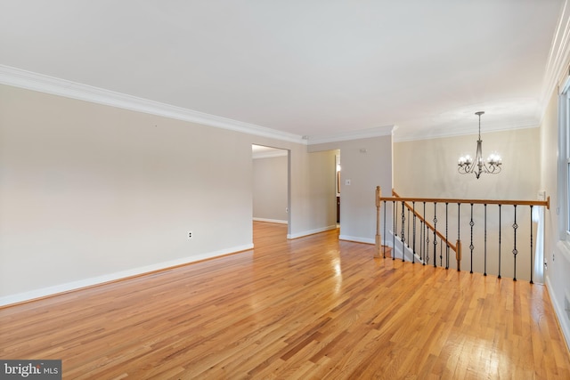 spare room featuring ornamental molding, baseboards, light wood-type flooring, and a chandelier