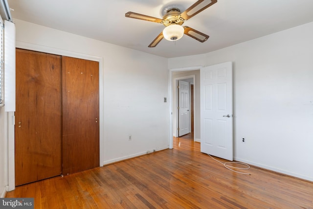 unfurnished bedroom featuring a closet, baseboards, hardwood / wood-style floors, and a ceiling fan