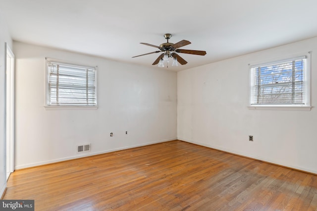 spare room with a wealth of natural light, visible vents, ceiling fan, and hardwood / wood-style flooring