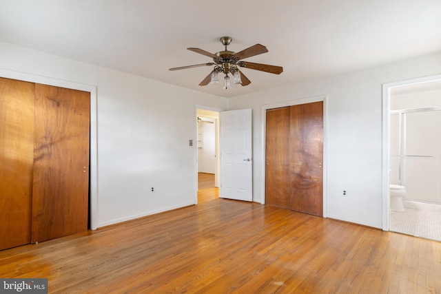 unfurnished bedroom featuring baseboards, multiple closets, hardwood / wood-style flooring, ensuite bath, and a ceiling fan