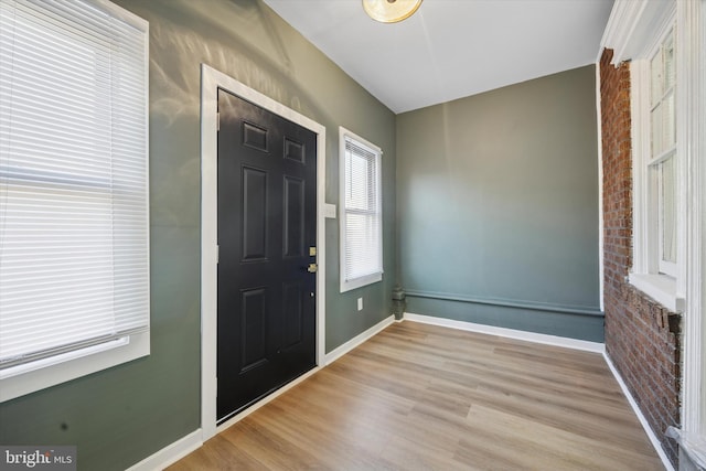 entrance foyer featuring baseboards, wood finished floors, and brick wall