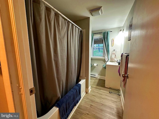 full bathroom with visible vents, wood finished floors, shower / bath combination with curtain, baseboard heating, and vanity